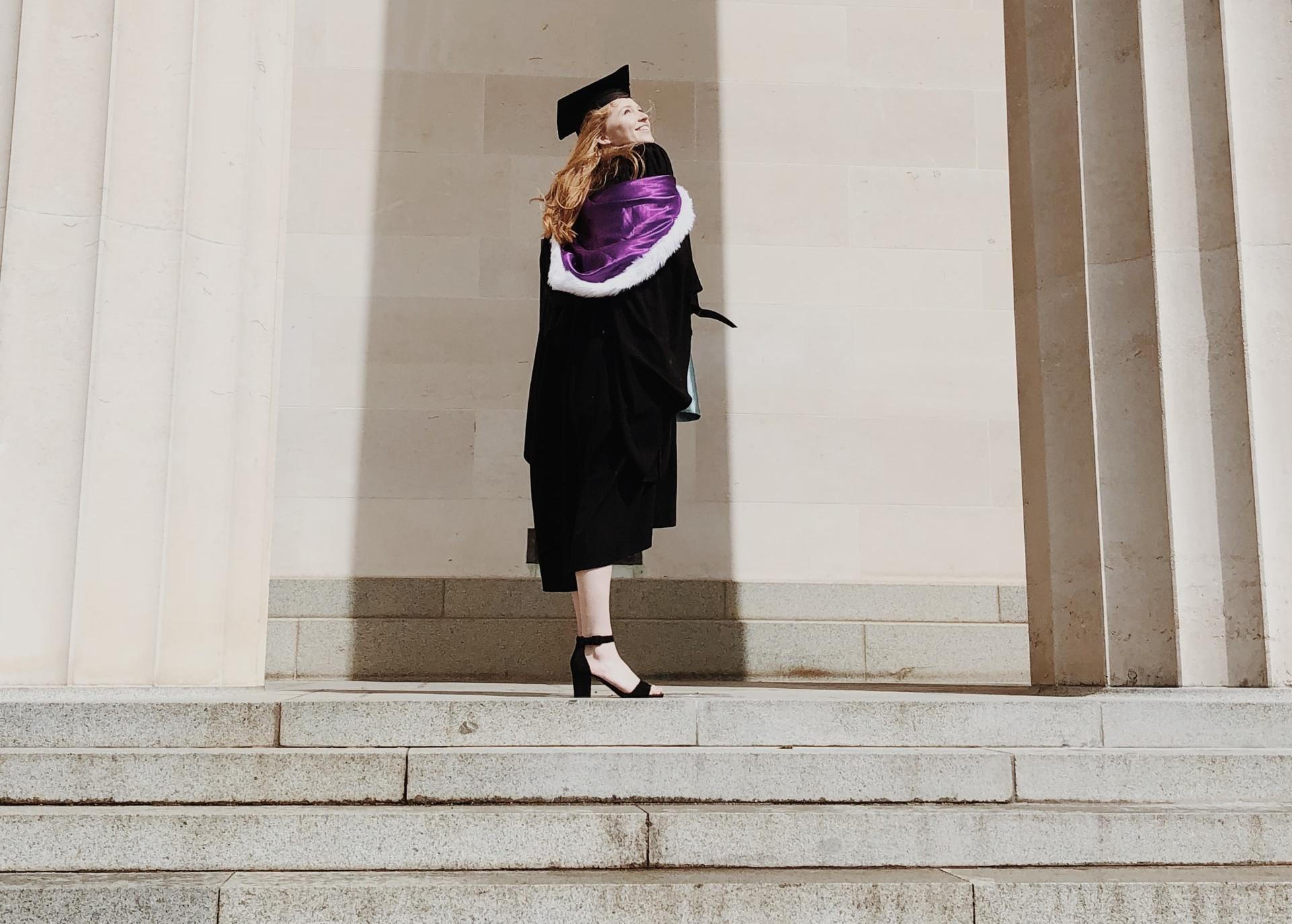 woman in academic regalia standing near concrete stairs