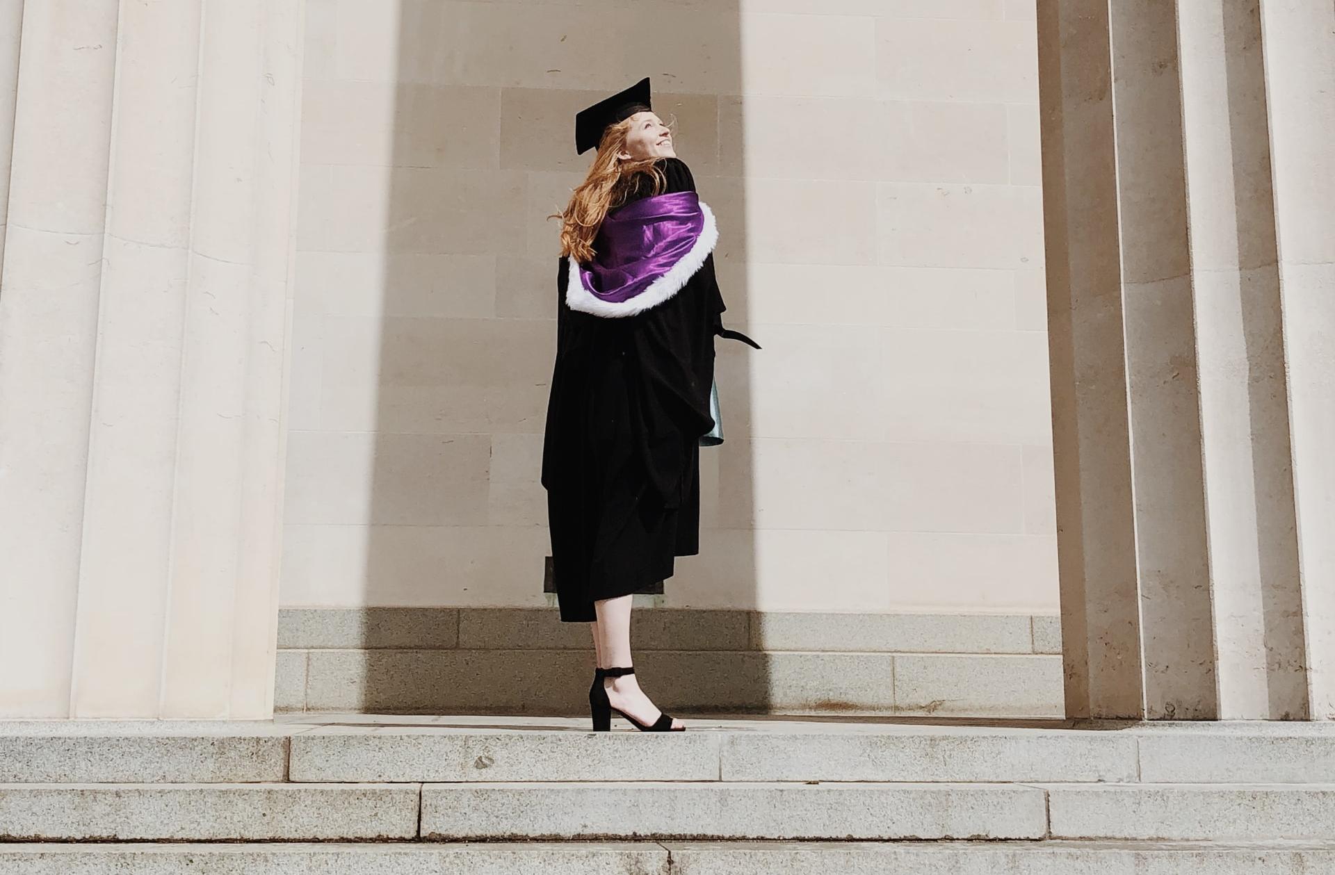 woman in academic regalia standing near concrete stairs