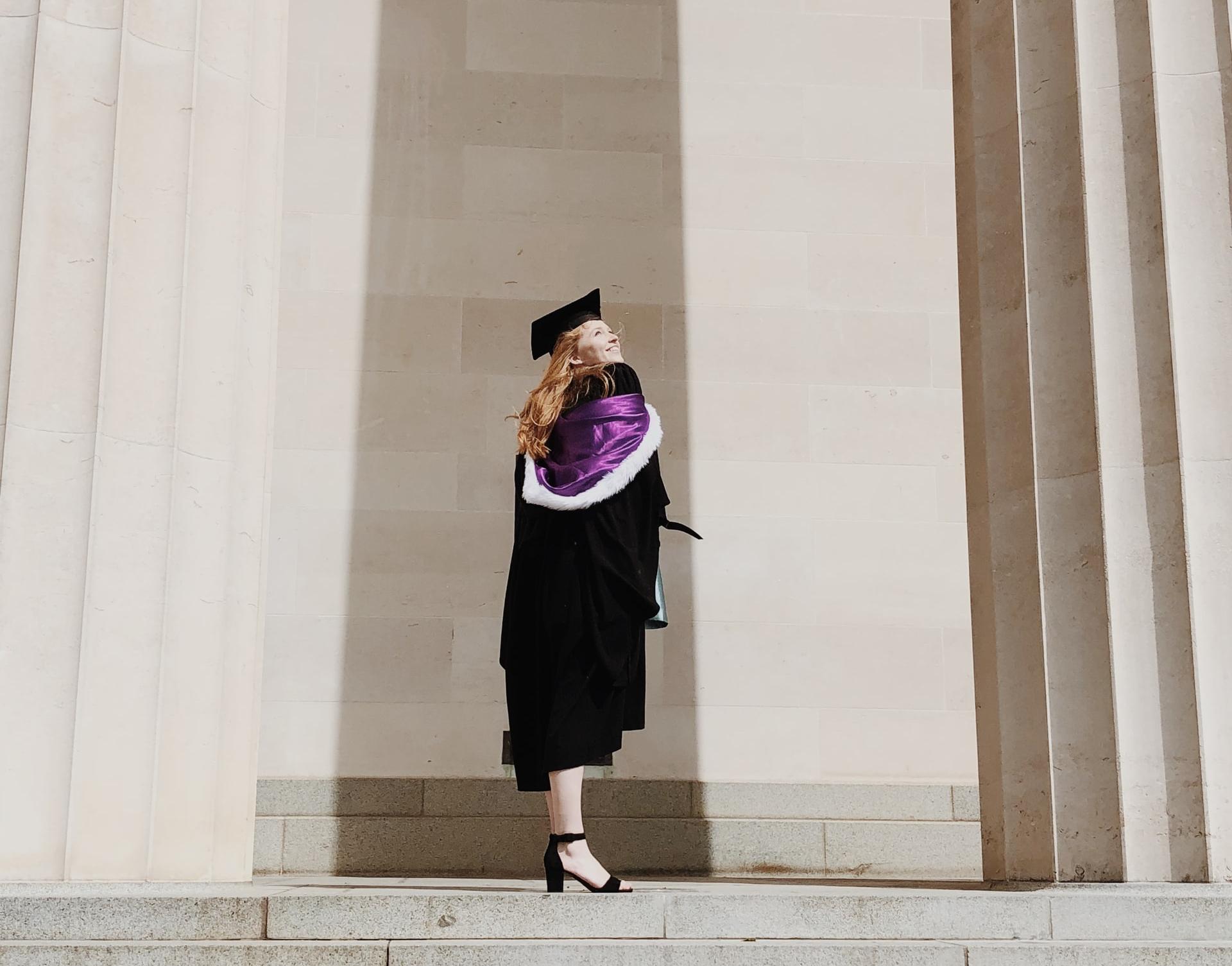 woman in academic regalia standing near concrete stairs